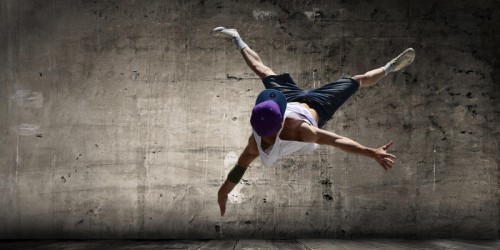 A break dancer is upside down in the air, forming an X with his arms and legs